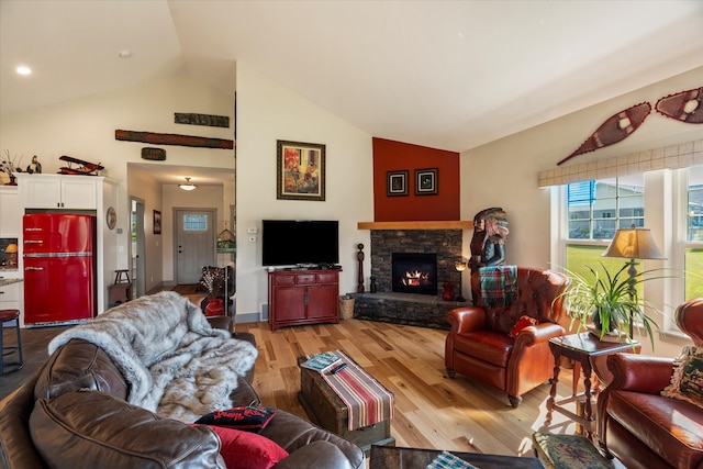 living room with lofted ceiling, a stone fireplace, and light hardwood / wood-style floors