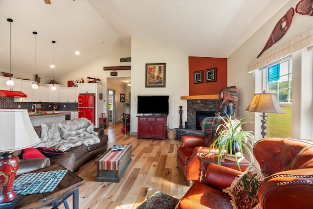 living room featuring light wood-type flooring, high vaulted ceiling, sink, and a stone fireplace