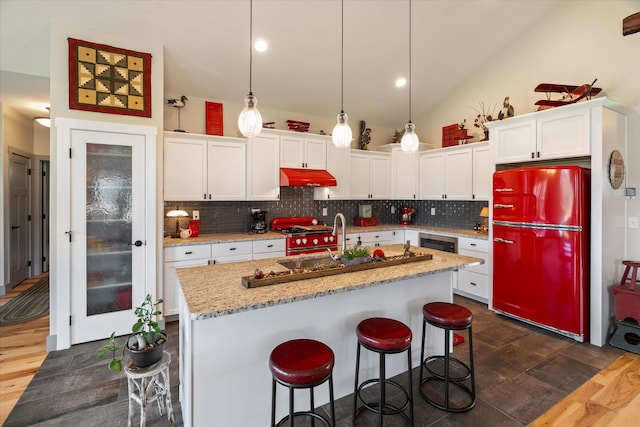 kitchen with a kitchen island with sink, decorative light fixtures, fridge, vaulted ceiling, and white cabinets