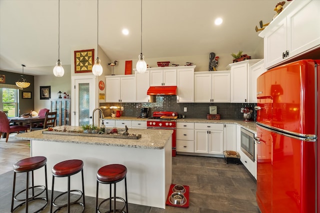 kitchen featuring decorative light fixtures, appliances with stainless steel finishes, a center island with sink, and white cabinetry