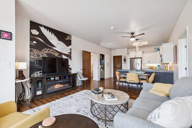 living room featuring dark wood-style flooring, a glass covered fireplace, and a ceiling fan