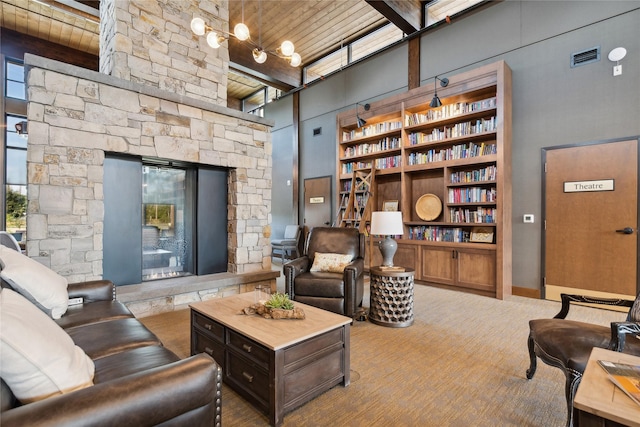 interior space with visible vents, a towering ceiling, wood ceiling, a stone fireplace, and beamed ceiling