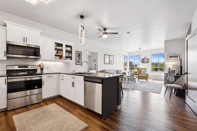 kitchen featuring open floor plan, dark wood-type flooring, a peninsula, stainless steel appliances, and a sink