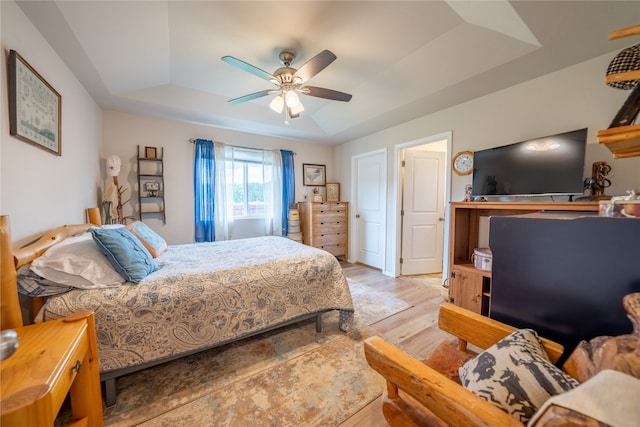 bedroom with a raised ceiling, ceiling fan, and light hardwood / wood-style flooring