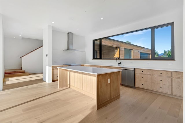 kitchen with dishwasher, a center island, wall chimney range hood, and light hardwood / wood-style flooring