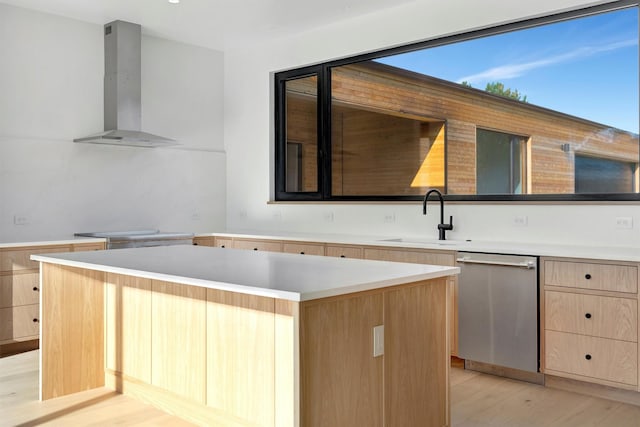 kitchen featuring wall chimney range hood, sink, stainless steel dishwasher, light hardwood / wood-style floors, and a kitchen island