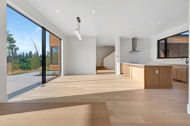 kitchen featuring sink, wall chimney range hood, decorative light fixtures, light hardwood / wood-style floors, and a kitchen island