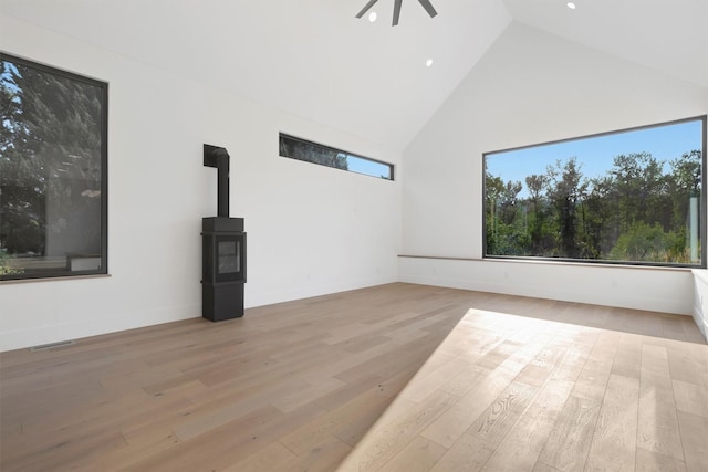 unfurnished living room featuring ceiling fan, light hardwood / wood-style floors, a wood stove, and high vaulted ceiling