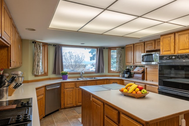 kitchen with a sink, stainless steel appliances, brown cabinetry, light countertops, and a center island
