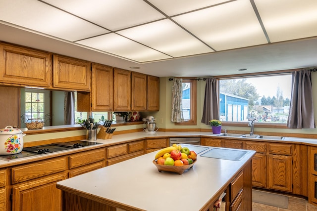 kitchen with stovetop with downdraft, a sink, brown cabinetry, and light countertops
