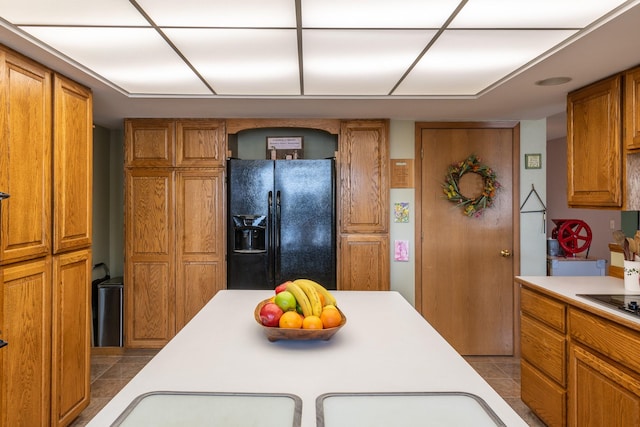 kitchen featuring black fridge, brown cabinets, light countertops, and tile patterned flooring