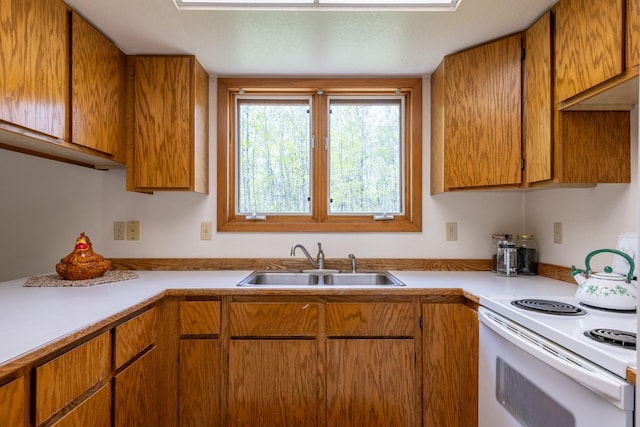 kitchen with a sink, white range with electric stovetop, light countertops, and brown cabinetry