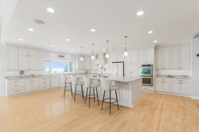 kitchen with pendant lighting, white cabinetry, a kitchen island, double oven, and light hardwood / wood-style floors