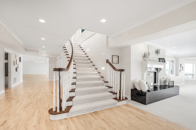 stairs featuring wood-type flooring, crown molding, and a premium fireplace