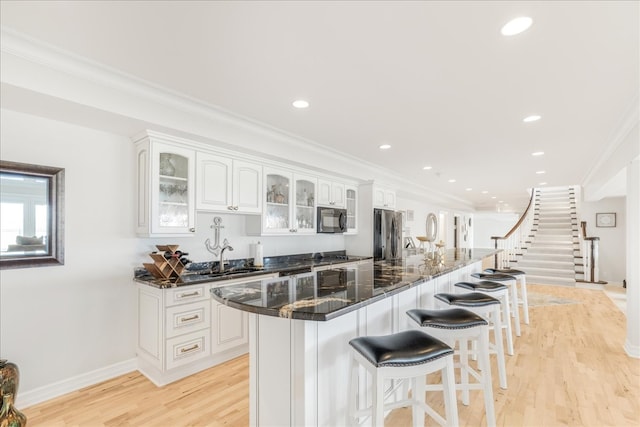 kitchen with white cabinets, a center island, crown molding, light hardwood / wood-style flooring, and dark stone counters