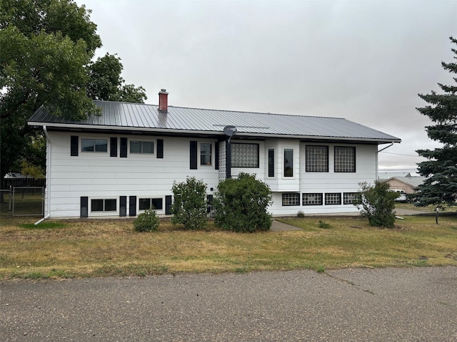 view of front facade featuring a front lawn, a chimney, fence, and metal roof