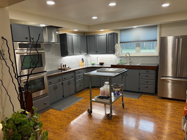 kitchen featuring wall chimney range hood, appliances with stainless steel finishes, dark countertops, and wood finished floors