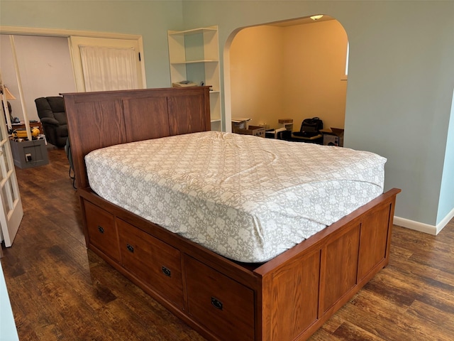 bedroom featuring baseboards, arched walkways, and dark wood finished floors