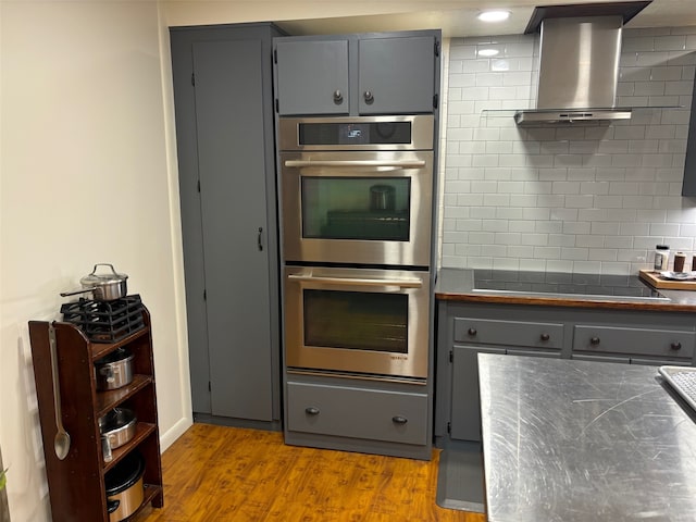 kitchen featuring gray cabinetry, stainless steel double oven, light hardwood / wood-style flooring, black electric cooktop, and tasteful backsplash