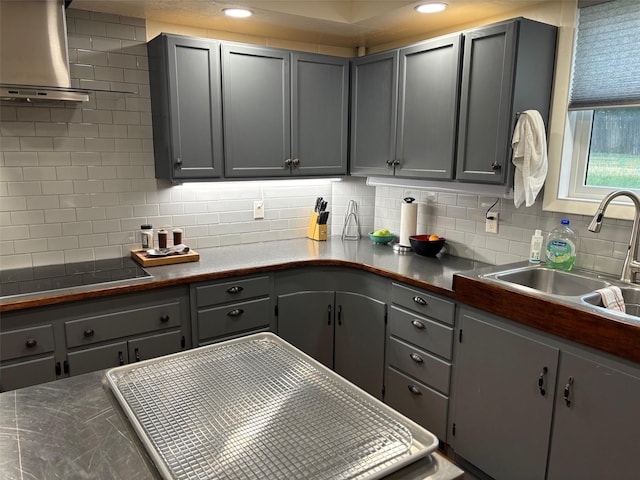 kitchen featuring dark countertops, black electric stovetop, gray cabinets, wall chimney range hood, and a sink