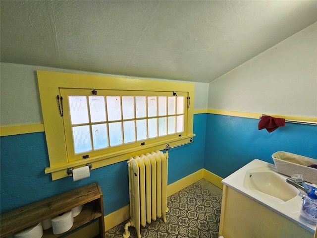 bathroom with a textured ceiling, radiator heating unit, vanity, and vaulted ceiling