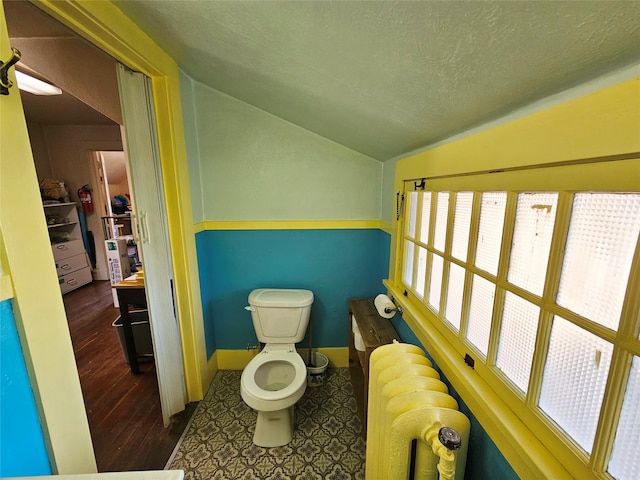 bathroom with radiator, a textured ceiling, hardwood / wood-style floors, toilet, and lofted ceiling