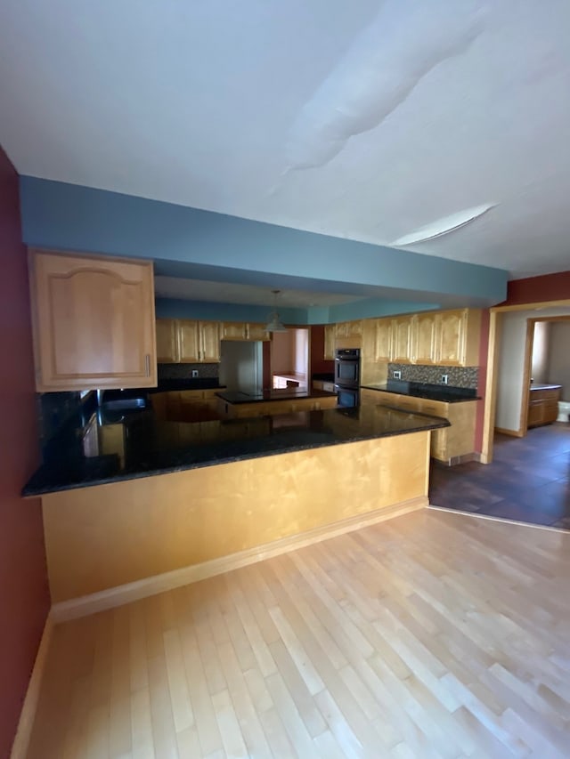 kitchen with kitchen peninsula, stainless steel refrigerator, hardwood / wood-style floors, and decorative backsplash