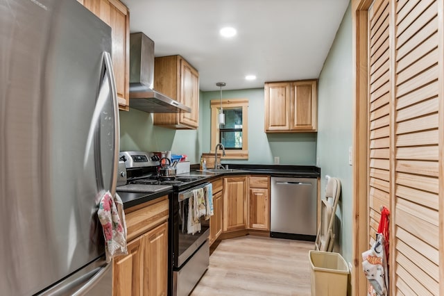 kitchen with pendant lighting, stainless steel appliances, wall chimney range hood, sink, and light hardwood / wood-style floors