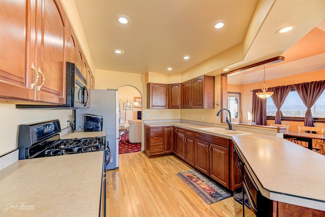 kitchen with decorative light fixtures, black appliances, kitchen peninsula, sink, and light hardwood / wood-style floors