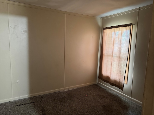 unfurnished room featuring dark colored carpet and ornamental molding