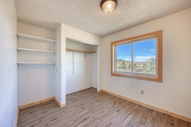 unfurnished bedroom with light hardwood / wood-style floors, a textured ceiling, and a closet