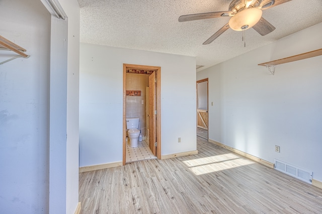 unfurnished bedroom with a textured ceiling, light wood-type flooring, ensuite bath, and ceiling fan