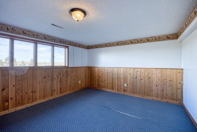 carpeted empty room featuring wood walls and a textured ceiling