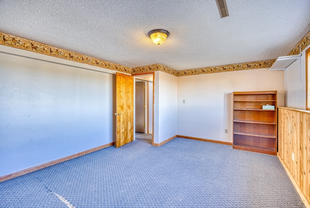 unfurnished bedroom featuring wood walls, a textured ceiling, and carpet flooring