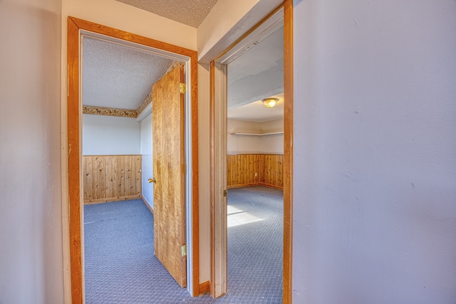 corridor featuring carpet flooring, wood walls, and a textured ceiling