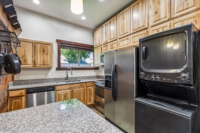 kitchen featuring appliances with stainless steel finishes, stacked washer and dryer, and sink