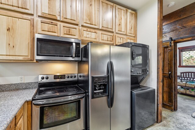 kitchen featuring stacked washer and dryer, a barn door, light brown cabinets, and appliances with stainless steel finishes