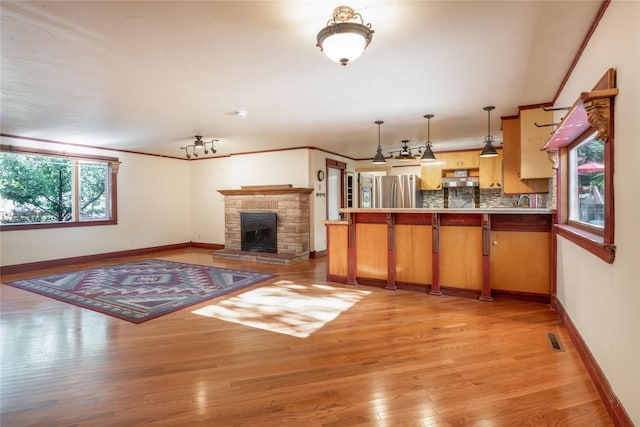 kitchen featuring kitchen peninsula, stainless steel fridge, pendant lighting, light hardwood / wood-style flooring, and a stone fireplace