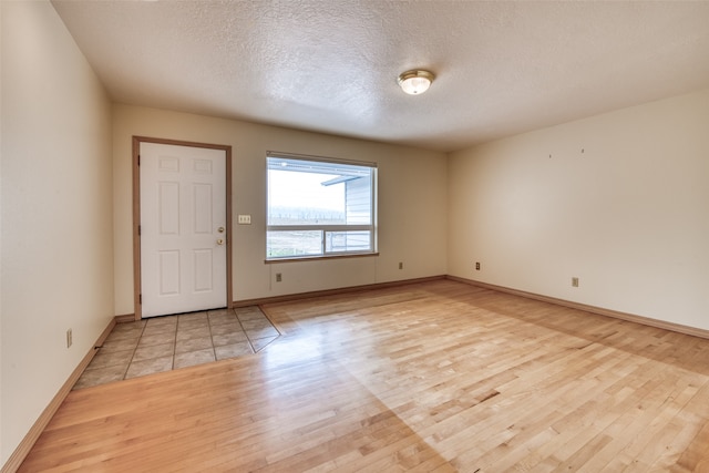 empty room with a textured ceiling and light hardwood / wood-style flooring