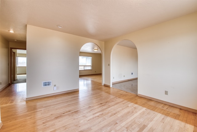 empty room with a textured ceiling and light hardwood / wood-style flooring