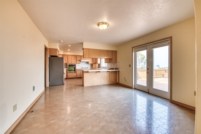 kitchen with appliances with stainless steel finishes, a textured ceiling, tasteful backsplash, and kitchen peninsula