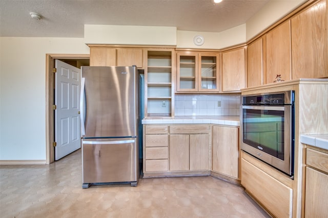 kitchen featuring appliances with stainless steel finishes, backsplash, light brown cabinets, a textured ceiling, and tile counters