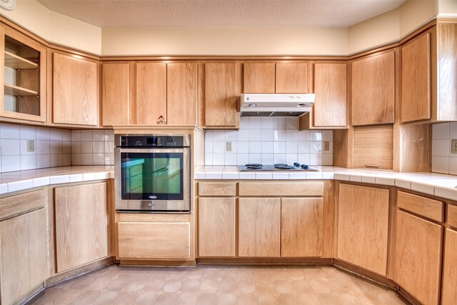 kitchen with tasteful backsplash, a textured ceiling, oven, tile countertops, and white stovetop