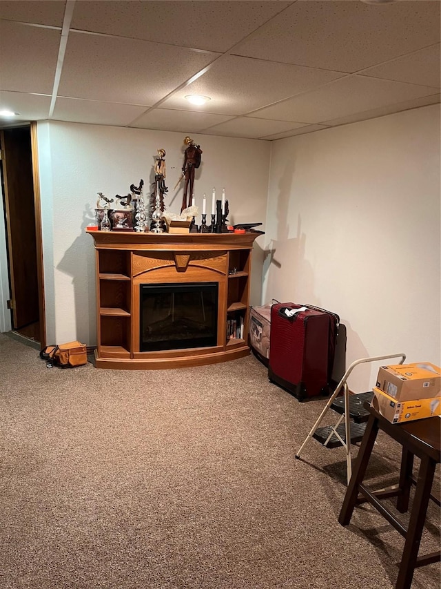 carpeted living area featuring a glass covered fireplace and a drop ceiling