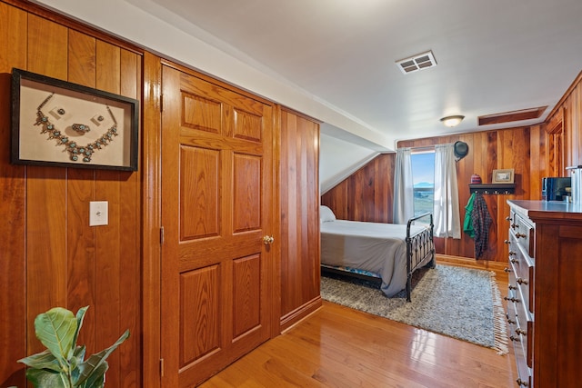 bedroom featuring wood walls, light hardwood / wood-style floors, and vaulted ceiling