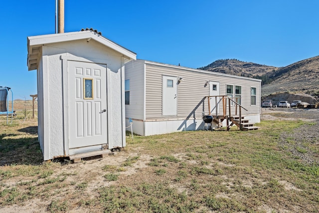 rear view of house with a trampoline, a mountain view, a lawn, and a storage unit