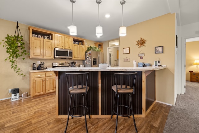 kitchen featuring light wood-type flooring, a breakfast bar, light brown cabinets, decorative light fixtures, and stainless steel appliances