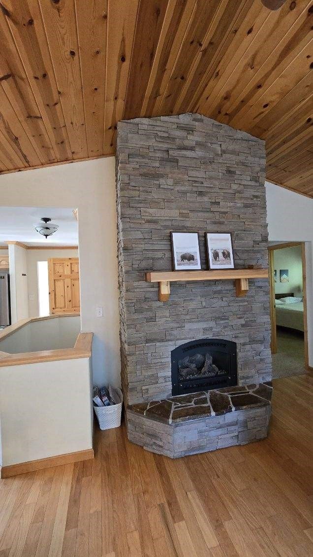 unfurnished living room with lofted ceiling, wood-type flooring, wood ceiling, and a fireplace