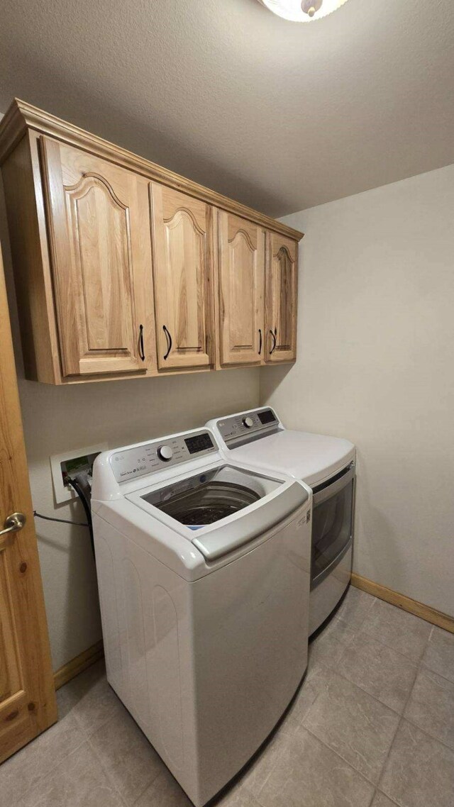 clothes washing area with a textured ceiling, cabinets, washing machine and dryer, and light tile patterned flooring