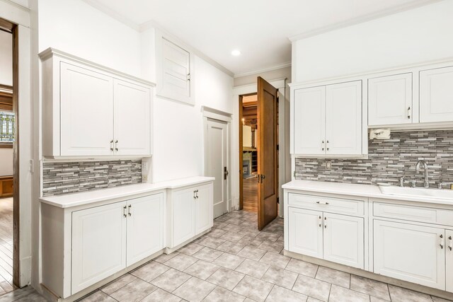 kitchen featuring ornamental molding, decorative backsplash, white cabinetry, and sink